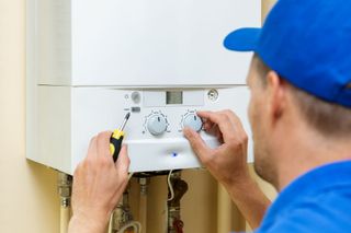 A gas boiler installer with blue hat fixing a boiler with a screwdriver