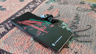 A smartphone showing a song by A Tribe Called Quest, next to the Edifier NeoBuds Pro earbuds