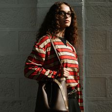 fashion week attendee wears glasses, red striped shirt, and brown handbag