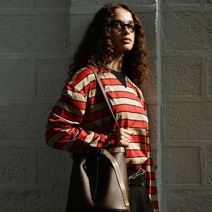 fashion week attendee wears glasses, red striped shirt, and brown handbag