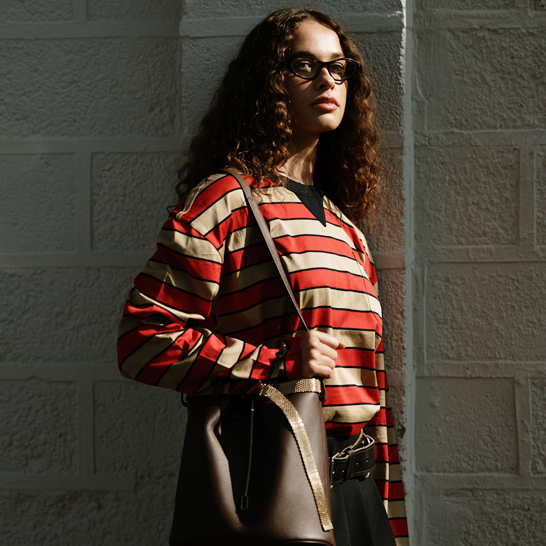 fashion week attendee wears glasses, red striped shirt, and brown handbag