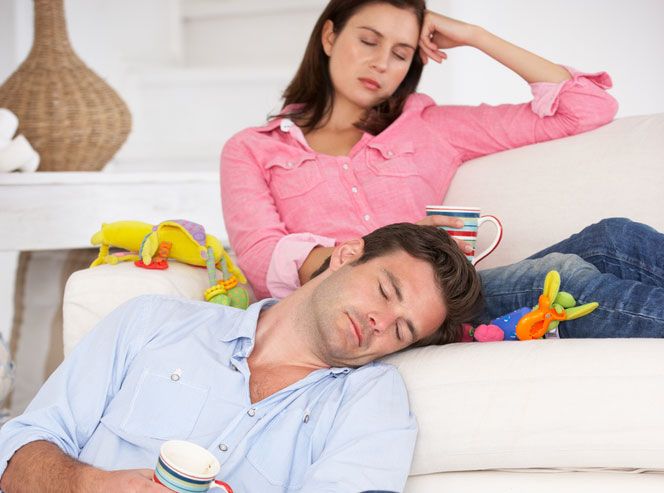 Parents sit in their living room, exhausted, amid children&#039;s toys strewn everywhere.