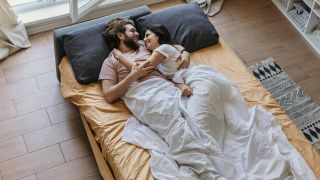 Man and woman cuddling in bed under a duvet