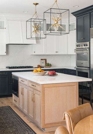 A wooden kitchen island with white worktop and two bowls of fruit in it, and white cabinets and a silver oven behind it