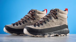 The Columbia Newton Alpine boots on a stone surface with a blue background