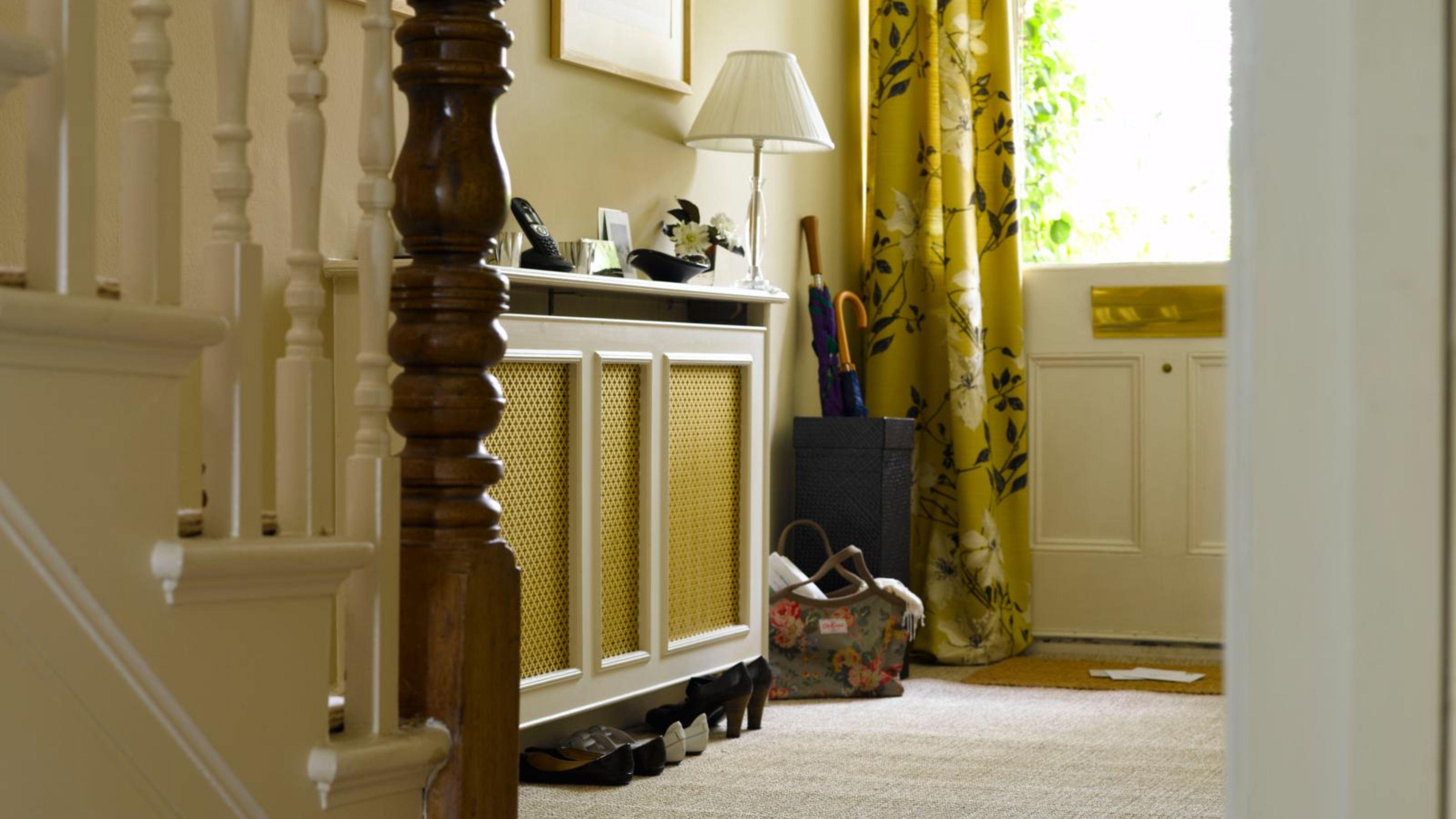 Small entryway area featuring a floor lamp, umbrella stand, and a breezy rattan-accent shoe storage cabinet
