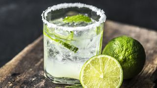 Caipirinha cocktail with slices of lime and salt on the rim, sat on wooden chopping board