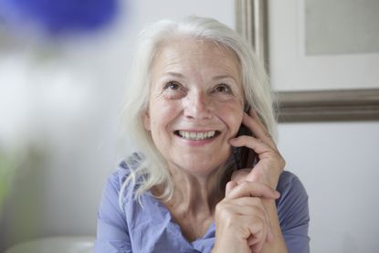 Happy senior woman looking up while answering mobile phone at home 
