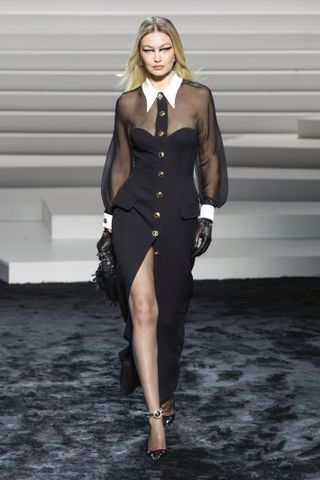 Gigi Hadid on the Versace fall 2024 runway wearing a black dress with sheer sleeves