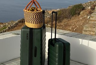 Photo of dark green suitcase and carry-on luggage on balcony overlooking Mediterranean sea.