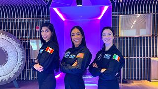 three astronauts standing in a row in flight suits, smiling with their hands crossed