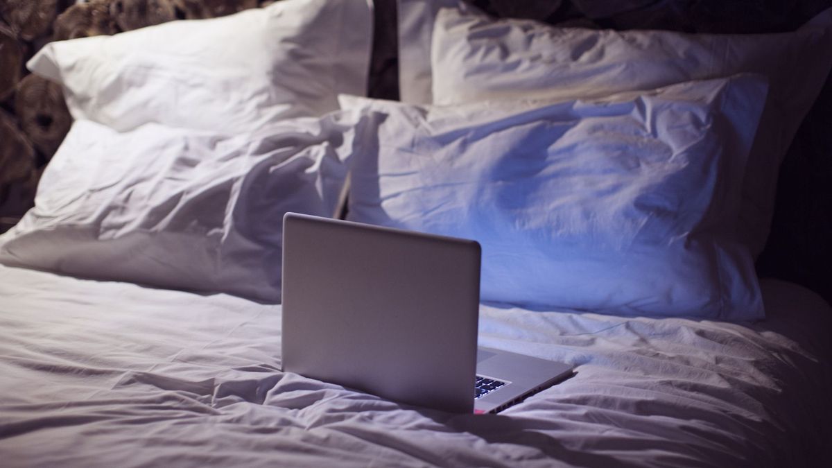 The image shows a laptop sitting open on a bed 