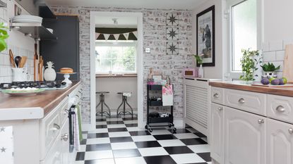 Exposed whitewashed brickwork of kitchen with large black and white checked floor tiles looking through doorway to breakfast bar and stools