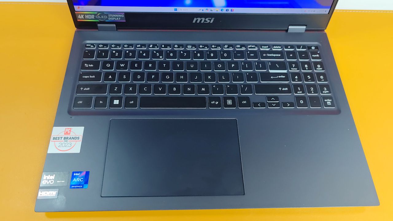 Top-down photo of a laptop to show its keyboard and touchpad against a yellow surface