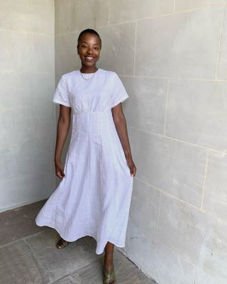 influencer Taffy Msipa smiles while posing in a minimalistic white short sleeve dress and green sandals