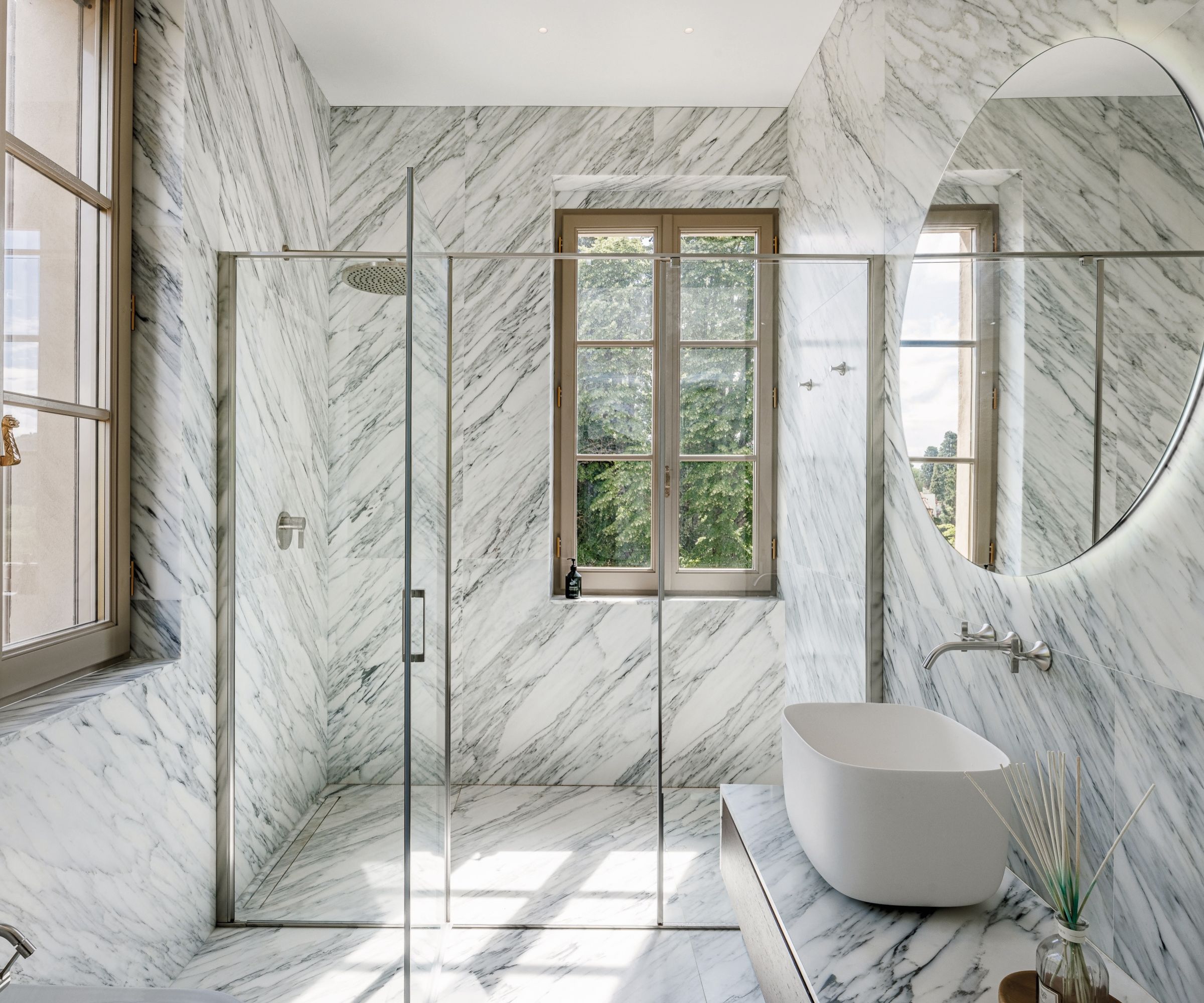 A light-filled marble bathroom with a walk-in glass shower, floating basin and oversized mirror, finished with clean lines and natural daylight.