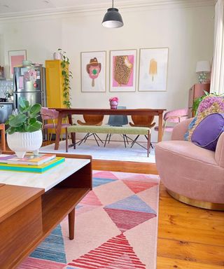 A small living room with a rug, seats, a dining table, and wall art