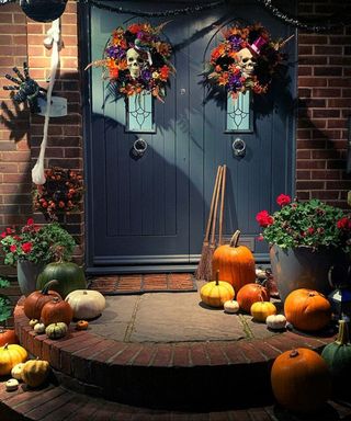 Halloween door decorating ideas with two skull door wreaths and assortment of pumpkins on and around navy painted front door