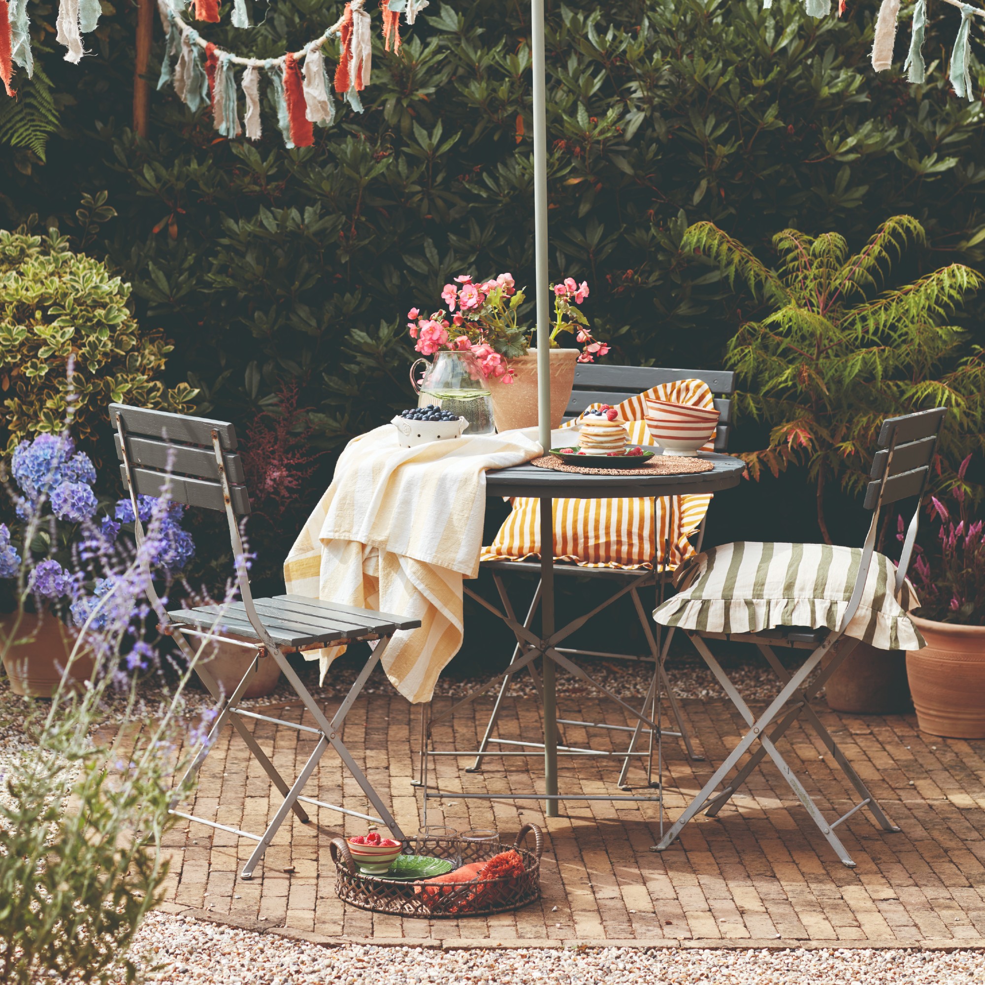 A garden with a metal bistro set, striped cushions and a colourful bunting hung above