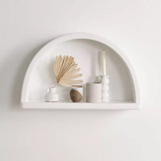 An arch-shaped wall shelf in white speckle finish with dried florals and other boho accessories