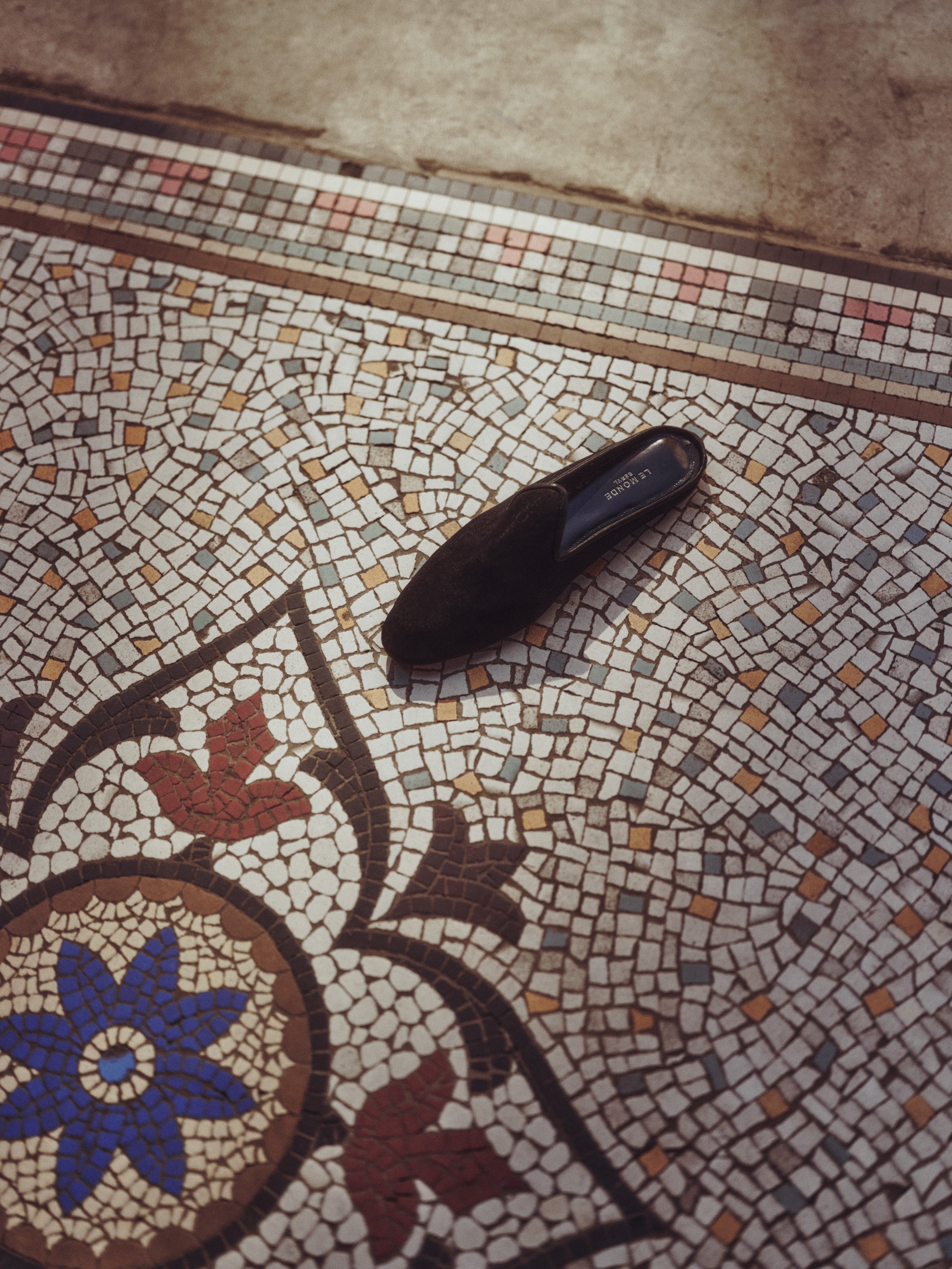 A tessellated mosaic floor with floral designs, topped by an abandoned velvet black mocasin shoe.