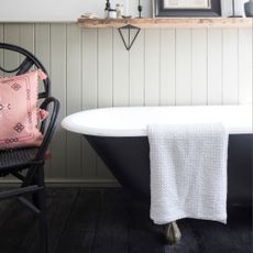 Black bathtub with towel hanging over, black rattan chair with cushion