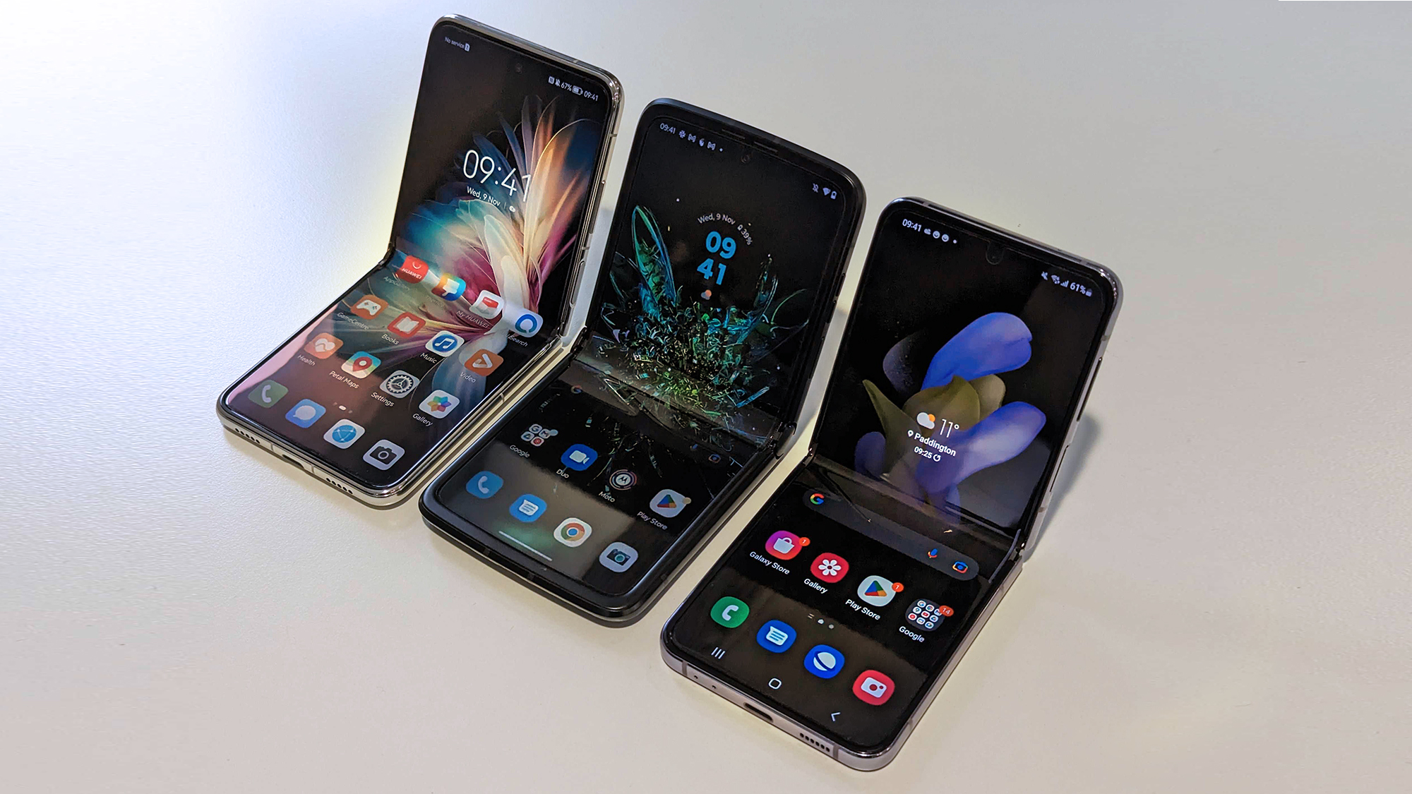 Motorola Razr 2022, Huawei P50 Pocket ja Samsung Galaxy Z Flip 4 vierekkäin pöydällä