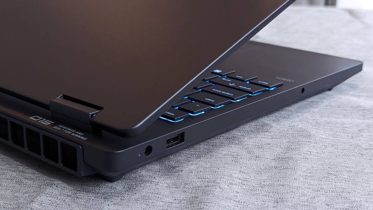 A partially open HyperX OMEN 15 laptop showing blue backlit arrow and modifier keys, along with visible side ports including USB and a headphone jack near the hinge.