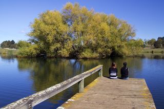 Two friends sitting on a wooden jetty on the edge of a lake