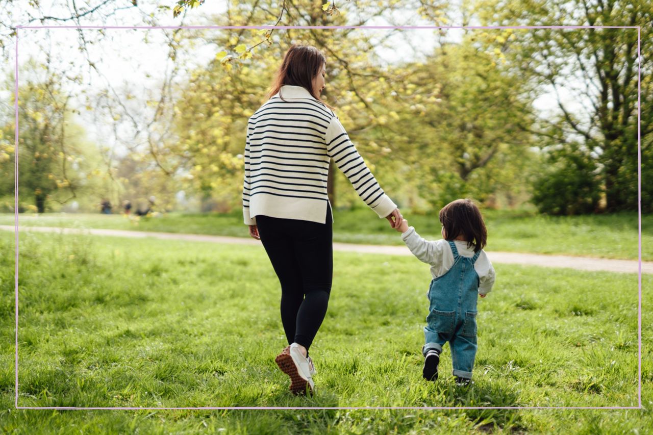 A woman and toddler holding hands while walking through a field