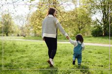 A woman and toddler holding hands while walking through a field