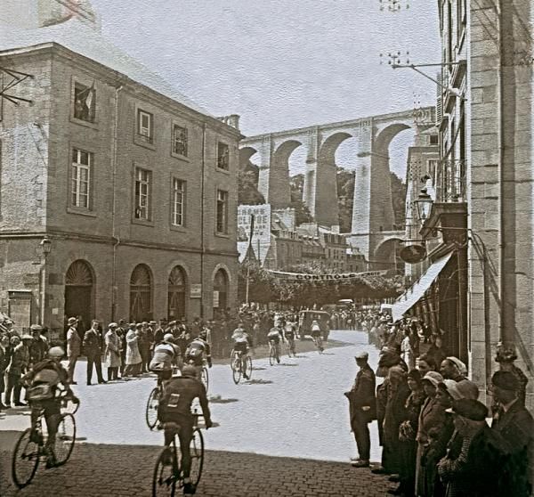 The peloton passes through a feeding station in the third stage of the 1930 Tour de France, from Dinan to Brest. In the western region of France, aqueducts are a reminder of a roman past. This Tour saw the innovation of a publicity caravan, conceived to fund the national teams introduced to counter the trade teams&rsquo; influence evident in previous Tours.