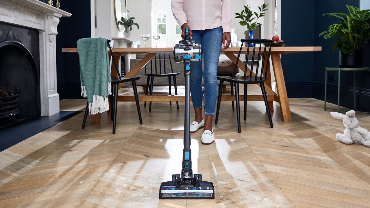 woman vacuuming up hair from wooden floorboards with Vax