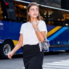 Amelie Zilber walks down the street in New York wearing a black pencil skirt with a t-shirt, heels and sheer socks.