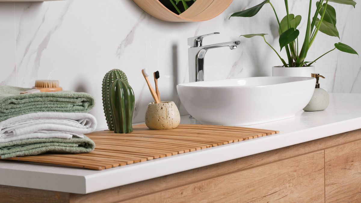 A bathroom interior, showing a sink, toothbrushes, towels and a plant