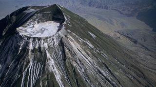 An aerial view of the summit crater of Ol Doinyo Lengai volcano with white streaks of dried lava running down the slopes.