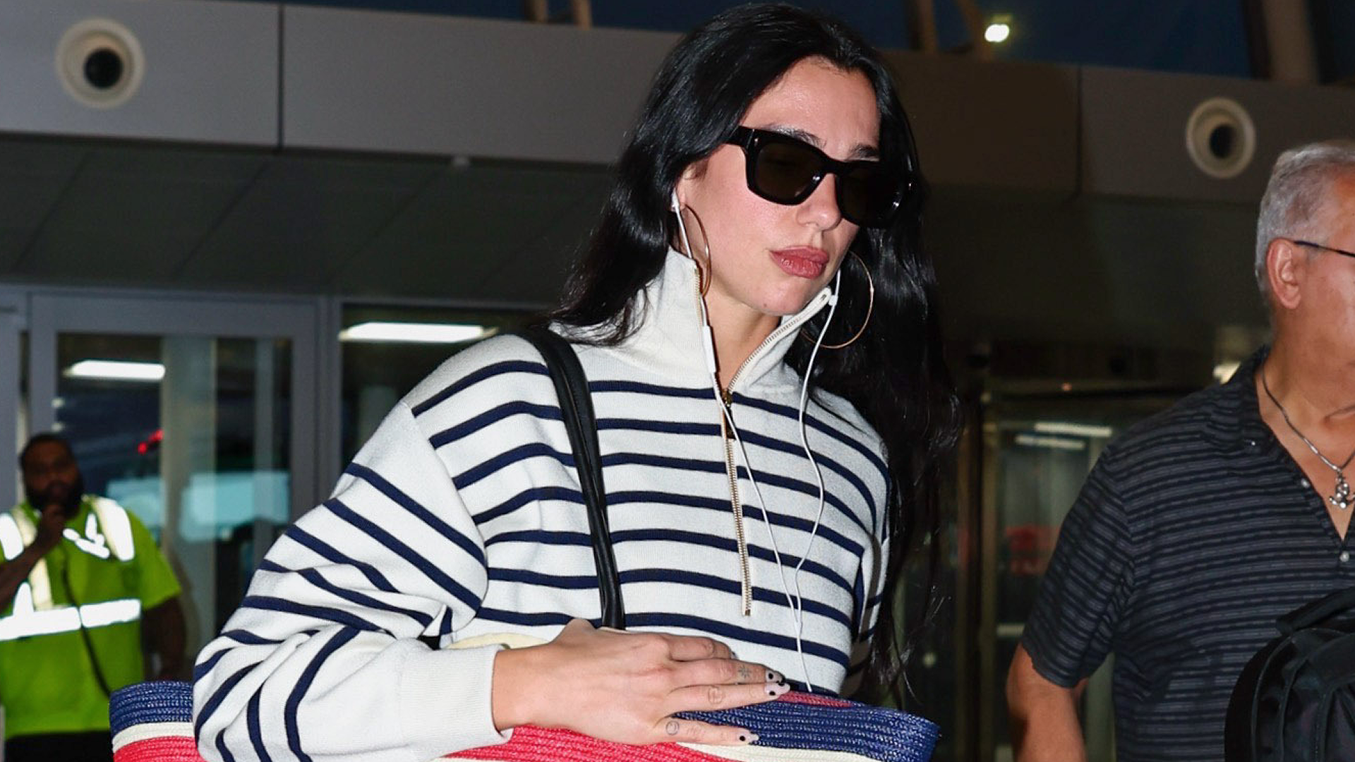 Dua Lipa arrived at the airport with Chanel's new oversized beach bag to match her coastal striped quarter-zip 