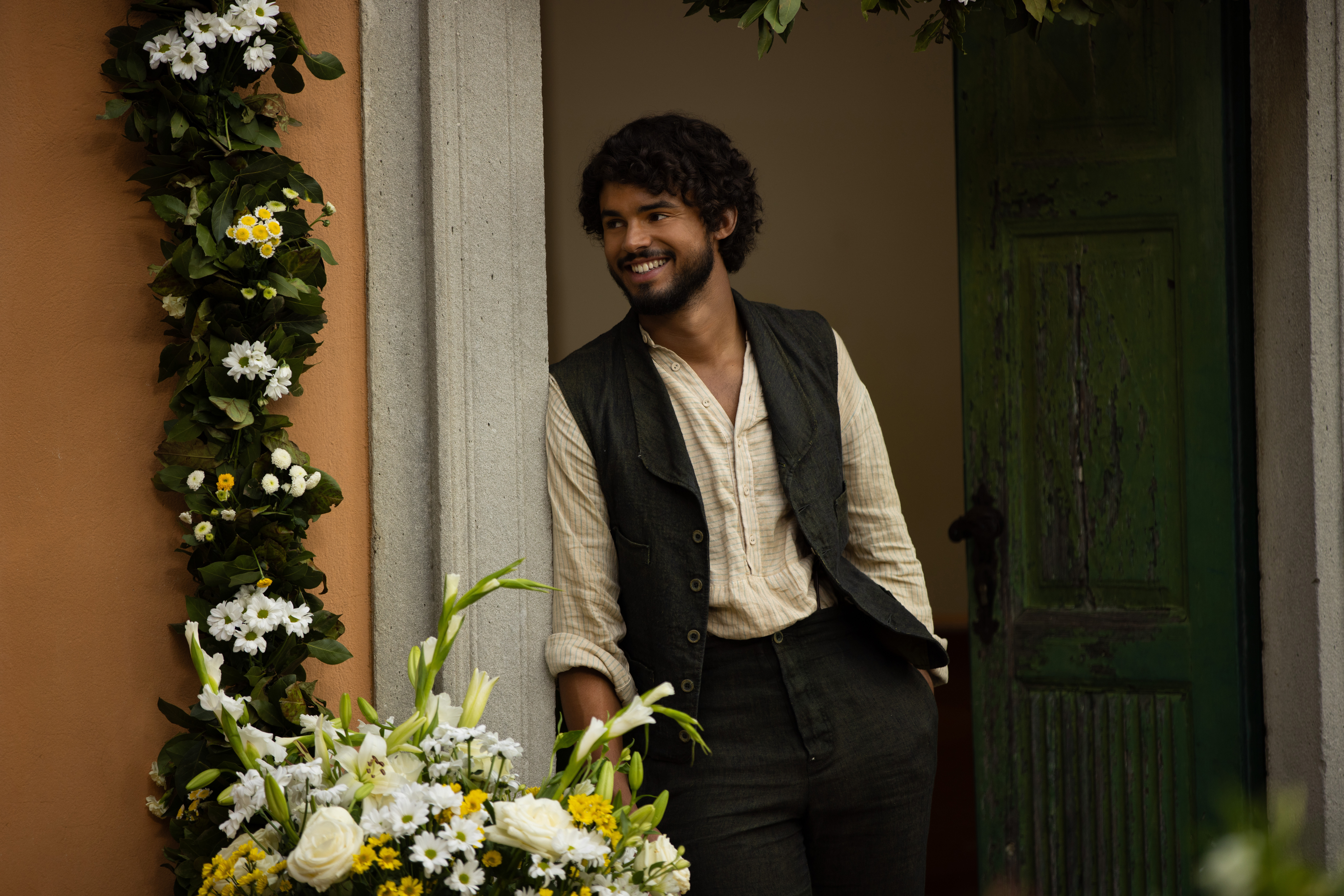 matthew broome as guy in the buccaneers season 2 leaning against a doorway by yellow flowers