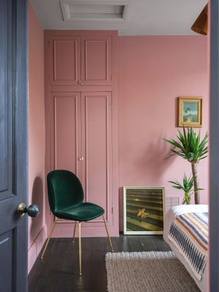 Bedroom with dark wood flooring, pink walls and wardrobe, and deep green chair