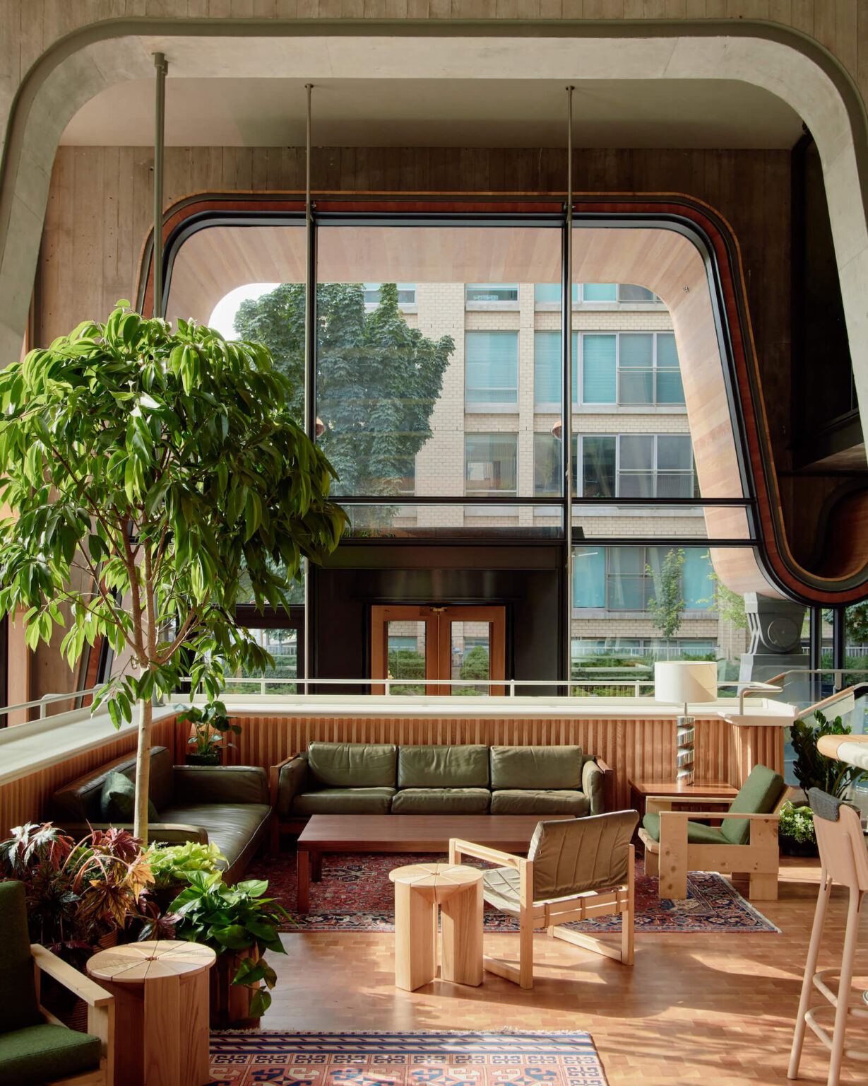 A sun-lit brutalist hotel lobby with mid-century modern furniture and plants.
