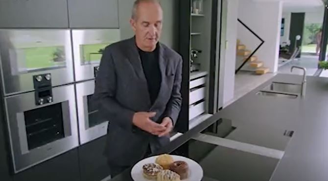 Kevin McCloud with a plate of cronuts and a naked man statue in the background