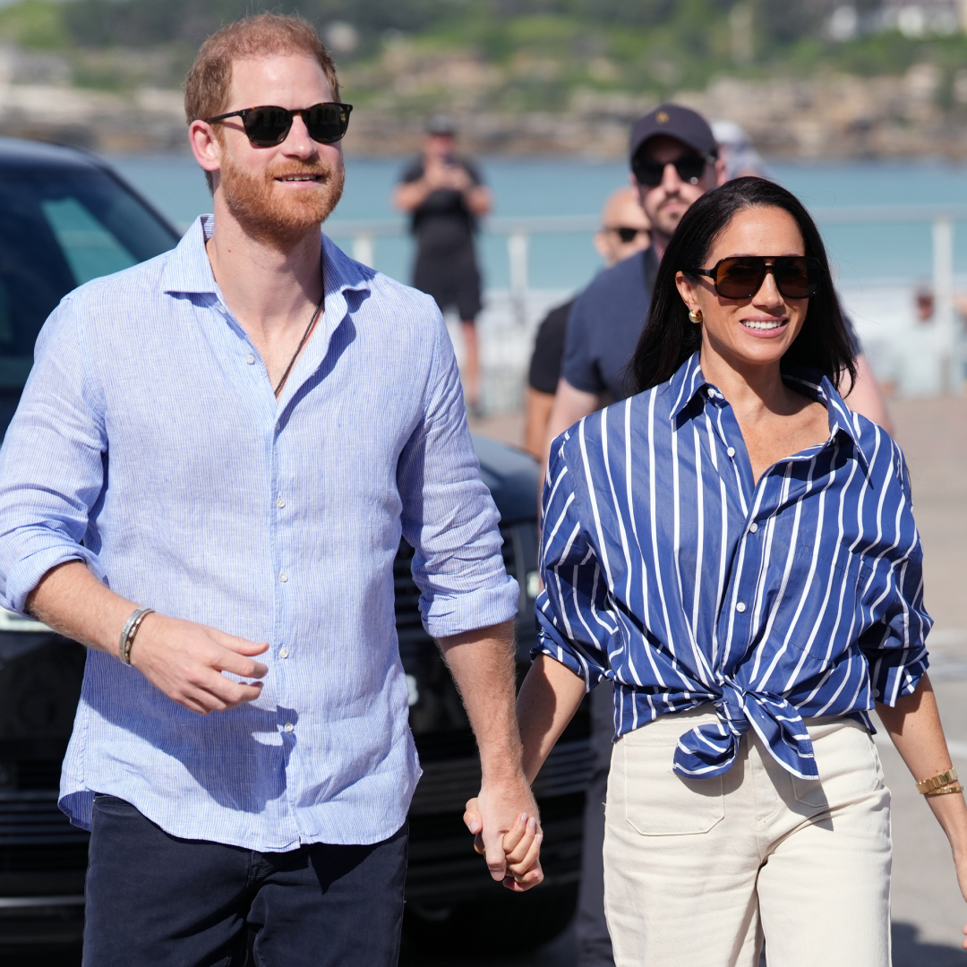 Prince Harry and Meghan Markle wearing sunglasses and blue shirts walking outside