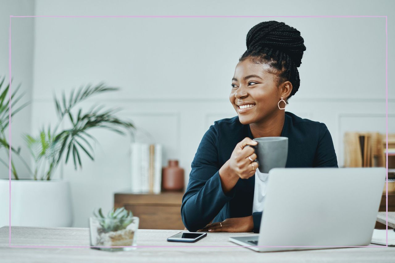 Smiling woman sat at a desk holding a coffee