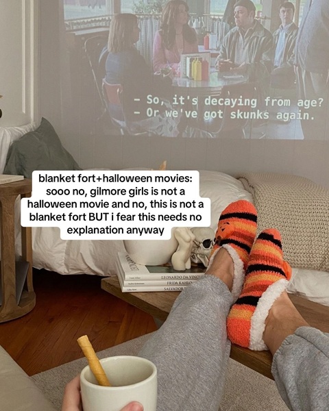 A person watching a show projected onto the wall with the text about making a blanket fort and watching your favourite halloween movies.