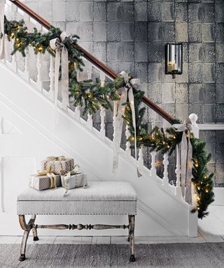 Christmas stair decor ideas with a pine garland looping along the banister, decorated with fairy lights and silver ribbons