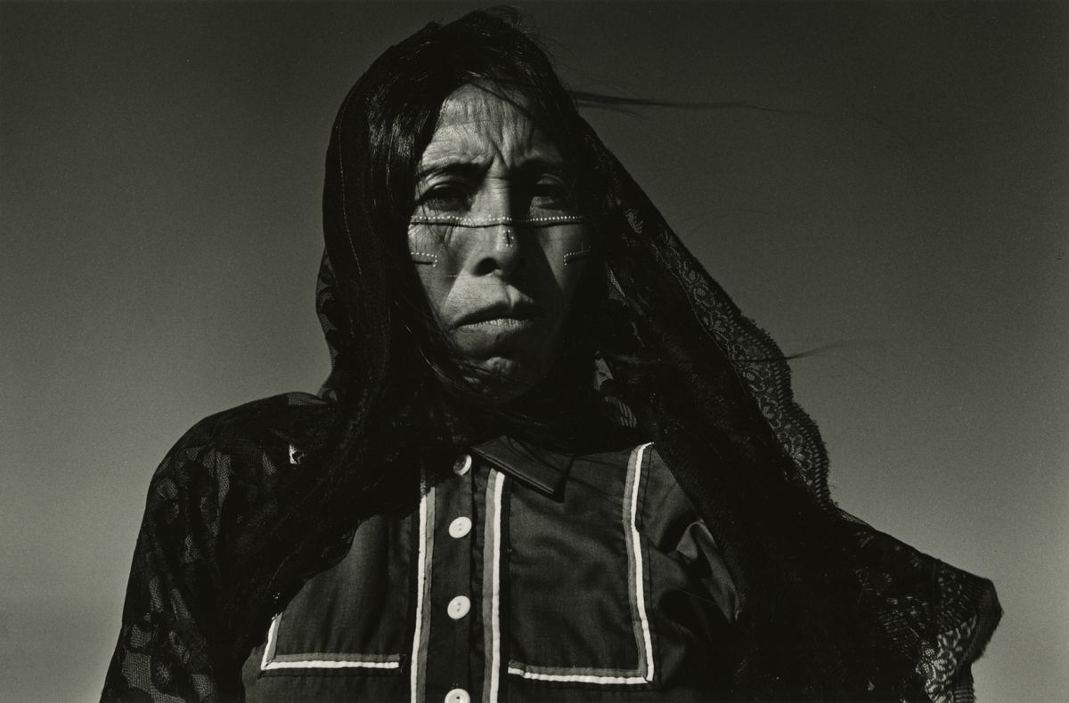 Little angel (Angelita), Sonoran Desert, Mexico, 1979. Courtesy of a Private Collection © Graciela Iturbide Alternative Text: Black and white portrait photograph of a woman with indigenous paintings on her face and a black veil over her head.