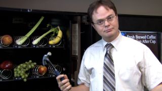 Dwight holding a hammer in front of. a vending machine full of fruits and vegetables in The Office