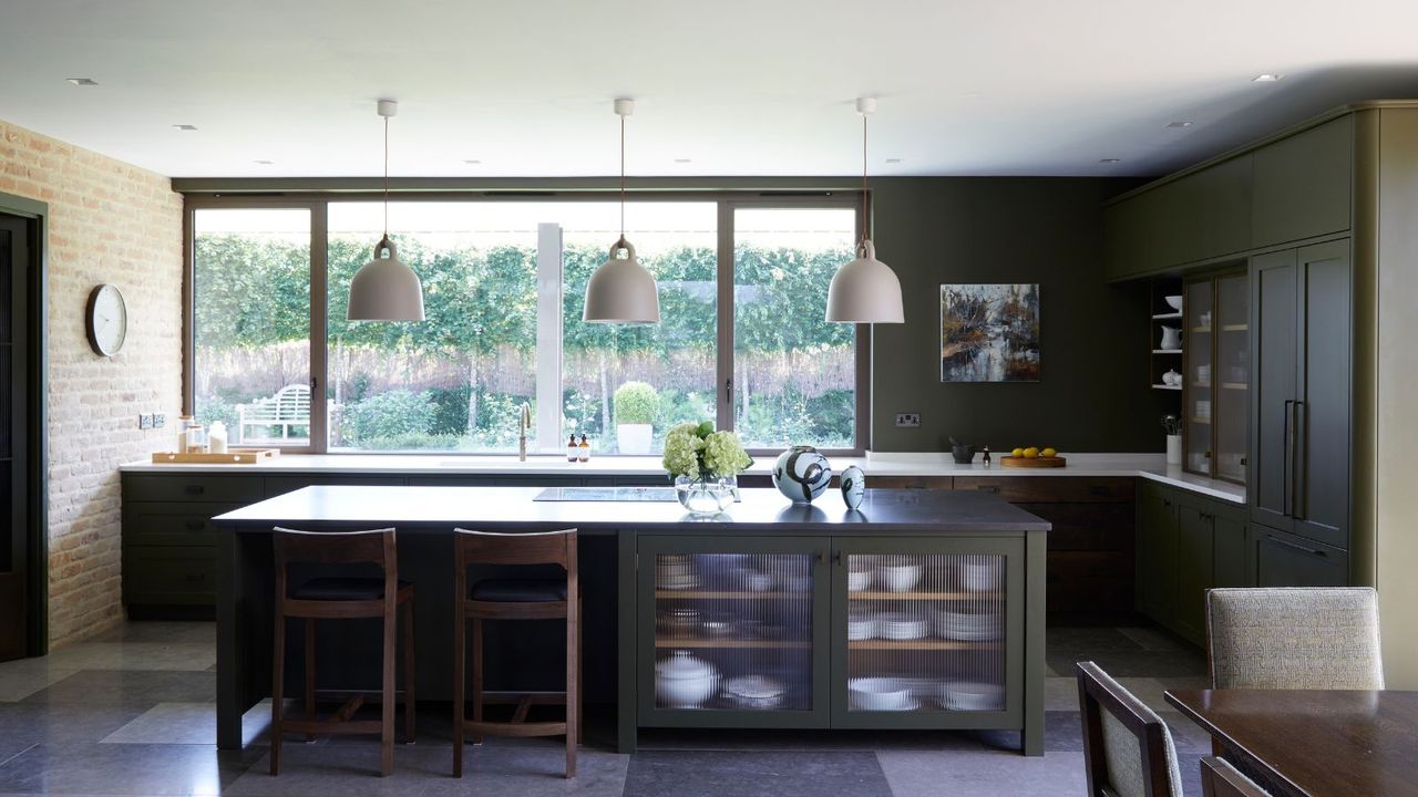 Kitchen with olive green cabinets and island, three pendant lights, tiled floor 