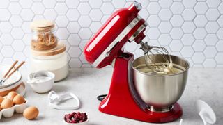 red KitchenAid stand mixer on bench with eggs and other utensils around it