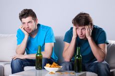 Two guys look bored while watching TV and drinking beer.